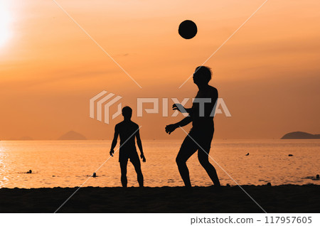 Silhouettes of Asian men playing beach football on beach by sea at sunset Silhouettes of Asian men playing beach football on beach by sea at sunset 117957605