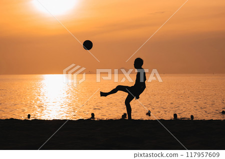 Silhouette of a man kicking a ball playing traditional Asian beach soccer on beach by the sea at sunset Silhouette of a man kicking a ball playing traditional Asian beach soccer on beach by the sea at sunset 117957609