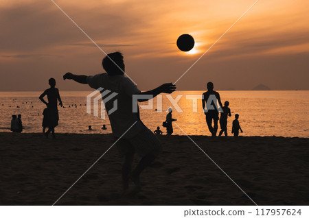 Silhouette of a man kicking a ball playing traditional Asian beach football on beach by the sea at sunset Silhouette of a man kicking a ball playing traditional Asian beach football on beach by the sea at sunset 117957624