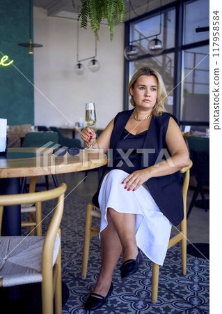 middle-aged plus size woman in old money style clothes drinking sparkling wine in a fancy restaurant middle-aged plus size woman in old money style clothes drinking sparkling wine in a fancy restaurant 117958584