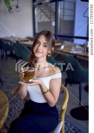 16-year-old teenage girl in old money style clothes drinks bumble coffee with an orange in a fancy restaurant 117958598
