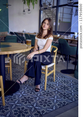 16-year-old teenage girl in old money style clothes drinks bumble coffee with an orange in a fancy restaurant 117958600