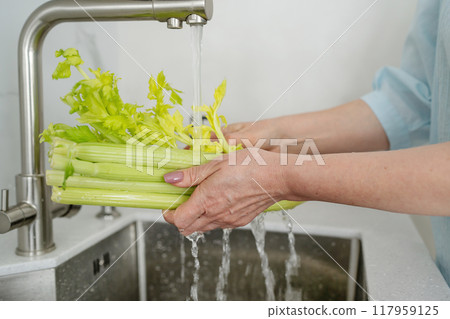 A woman is cleaning fresh vegetables in a modern kitchen to prepare a healthy meal A woman is cleaning fresh vegetables in a modern kitchen to prepare a healthy meal 117959125