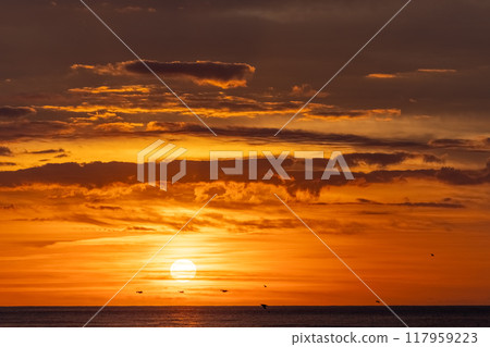 A stunning sunset over the ocean with dramatic clouds, birds flying, creating a serene scene A stunning sunset over the ocean with dramatic clouds, birds flying, creating a serene scene 117959223