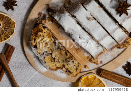 Slices of Christmas Stollen in Christmas lights and decoration. Traditional sweet fruit loaf with icing sugar festive pastry dessert. Holiday baking food 117959418
