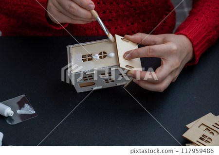 Unrecognizable woman in red sweater painting craft wooden houses for conscientious Merry Christmas decor. Sustainable celebration minimal responsible DIY holiday project. Step by step instruction Unrecognizable woman in red sweater painting craft wooden houses for conscientious Merry Christmas decor. Sustainable celebration minimal responsible DIY holiday project. Step by step instruction 117959486