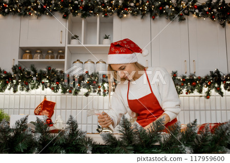 Young attractive woman wearing red apron and santa hat is holding icing sugar in her hands. 117959600