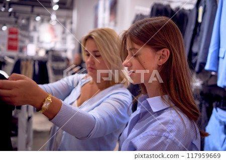 Mother and daughter shopping. A middle-aged plus-size woman and a teenage girl choose clothes and decor in a store. 117959669