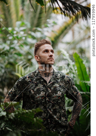 Handsome man with tattoo standing in botanical garden, in the middle of lush green foliage. Handsome man with tattoo standing in botanical garden, in the middle of lush green foliage. 117959946