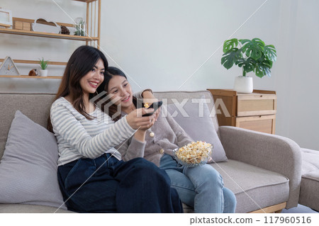 Lesbian couple enjoying movie night with popcorn Lesbian couple enjoying movie night with popcorn 117960516
