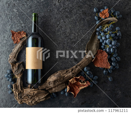 Bottle of red wine, blue grapes, and old vine snags on a black stone background. Bottle of red wine, blue grapes, and old vine snags on a black stone background. 117961211