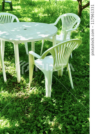 Garden chairs and a garden table in the sunlight filtering through the trees Garden chairs and a garden table in the sunlight filtering through the trees 117961331
