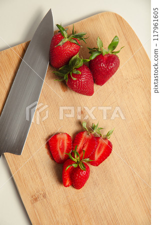 The strawberries are cut into slices. they lie on a wooden board and next to the knife 117961605