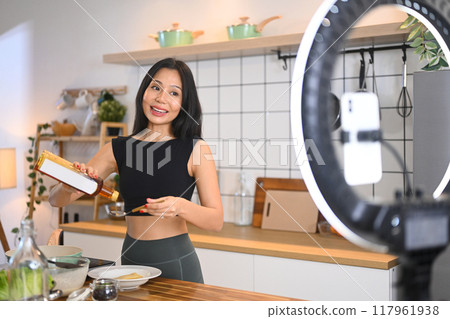 Young woman using smartphone on tripod for recording video healthy vegetable salad cooking tutorial Young woman using smartphone on tripod for recording video healthy vegetable salad cooking tutorial 117961938