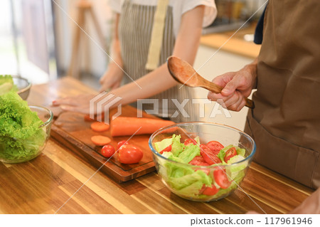 Cropped shot of young couple enjoys preparing a delicious and healthy salad together in a kitchen Cropped shot of young couple enjoys preparing a delicious and healthy salad together in a kitchen 117961946