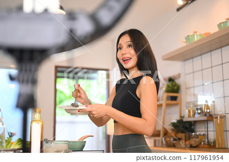 Young woman vlogger recording video cooking lesson about healthy vegetarian meal in modern kitchen Young woman vlogger recording video cooking lesson about healthy vegetarian meal in modern kitchen 117961954