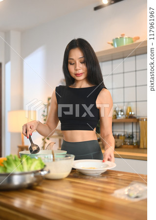 Young woman in sportswear preparing healthy meal in the kitchen with minimalistic design Young woman in sportswear preparing healthy meal in the kitchen with minimalistic design 117961967