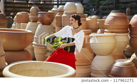 With confident pose, she holds her glass of wine aloft, proud smile on her lips against backdrop of carefully crafted pottery. Concept of vintage, art. 117962271