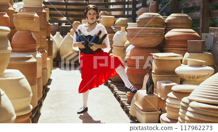 Woman enjoys glass of red wine, surrounded by shelves of ceramic pots, with peaceful expression on her face. Concept of tourism and art. 117962273