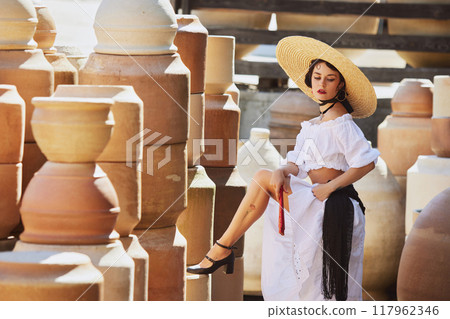 Young woman, elegantly stands in traditional pottery yard, capturing essence of Spain's cultural heritage and end of summer. Concept of harvesting. 117962346