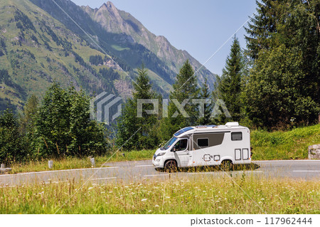 Scenic view big modern white family rv camper van vehicle drive Europe highway road alpine pass mountain sunny summer day. Rving motorhome lifestyle travel adventure tourism trip Alps journey concept 117962444