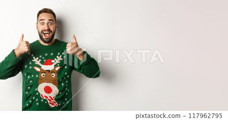 Christmas, holidays and celebration. Excited bearded guy in green sweater showing thumbs up, like something amazing, standing over white background Christmas, holidays and celebration. Excited bearded guy in green sweater showing thumbs up, like something amazing, standing over white background 117962795