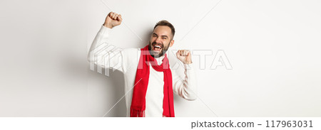 Happy bearded man celebrating christmas holidays on party, dancing and pointing fingers, standing over white background 117963031