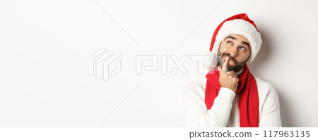 New Year party and winter holidays concept. Close-up of bearded man in Santa hat looking thoughtful at upper left corner, thinking or making decision, choosing christmas gift, white background New Year party and winter holidays concept. Close-up of bearded man in Santa hat looking thoughtful at upper left corner, thinking or making decision, choosing christmas gift, white background 117963135