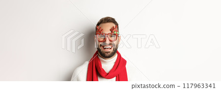 Christmas, New Year and celebration concept. Close-up of happy bearded man smiling, wearing party glasses and red scarf, white background Christmas, New Year and celebration concept. Close-up of happy bearded man smiling, wearing party glasses and red scarf, white background 117963341