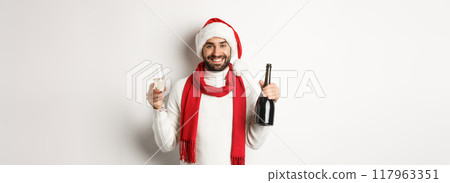 Christmas party and holidays concept. Happy bearded man in Santa hat, celebrating New Year, drinking champagne, standing over white background 117963351