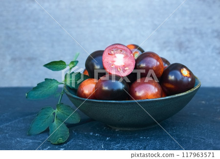 Black tomatoes of Indigo Rose in a bowl on the stone table. Black tomatoes of Indigo Rose in a bowl on the stone table. 117963571