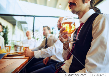 Colleagues, businessmen relaxing at the bar with beers, balancing work with bit of fun. Celebrating well-coordinated teamwork and success Colleagues, businessmen relaxing at the bar with beers, balancing work with bit of fun. Celebrating well-coordinated teamwork and success 117963752