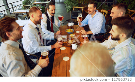 Colleagues, businessmen relaxing at the bar with beers, balancing work with bit of fun. Celebrating well-coordinated teamwork and success Colleagues, businessmen relaxing at the bar with beers, balancing work with bit of fun. Celebrating well-coordinated teamwork and success 117963753