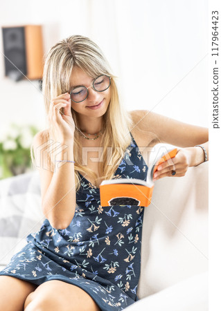 A young lady is reading a book and wearing prescription glasses. 117964423