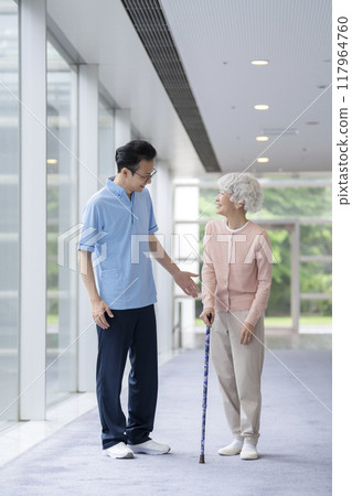 Senior woman walking with a cane and care staff 117964760