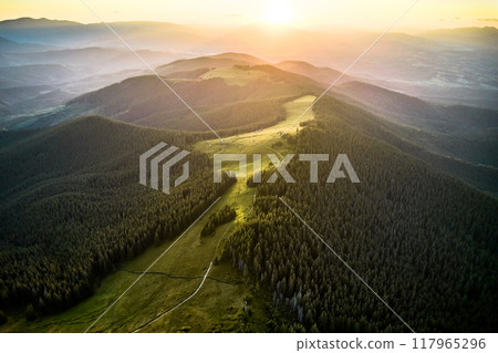 Breathtaking aerial view of mountain landscape at sunset. Golden light bathes rolling hills and lush forests, creating serene and idyllic scene. Distant mountains adding depth to picturesque vista. 117965296