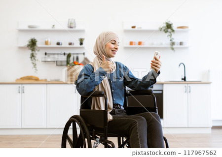Muslim woman in wheelchair taking selfie at home kitchen 117967562