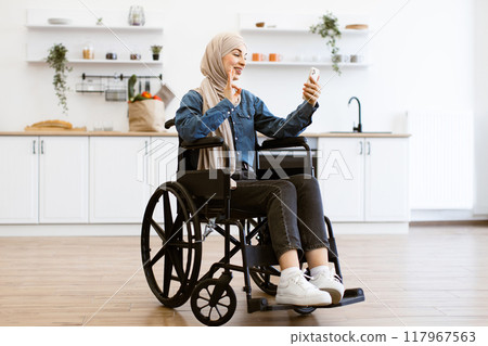 Muslim woman in wheelchair using smartphone at home 117967563
