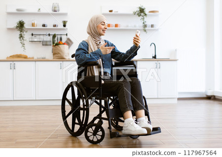 Muslim woman in wheelchair using mobile phone at home Muslim woman in wheelchair using mobile phone at home 117967564