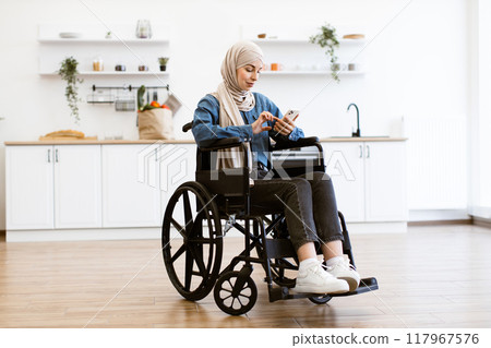 Muslim woman in wheelchair using smartphone at home kitchen 117967576