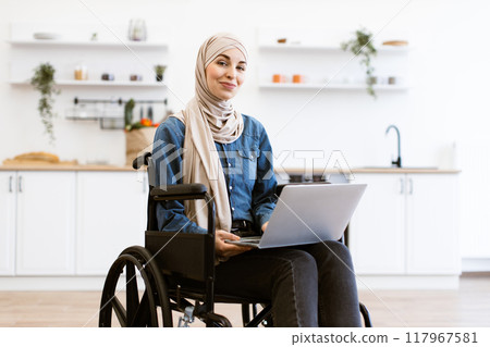 Muslim woman in wheelchair working on laptop at home 117967581