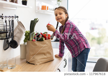 Smiling girl in kitchen with bag of fresh vegetables Smiling girl in kitchen with bag of fresh vegetables 117967618