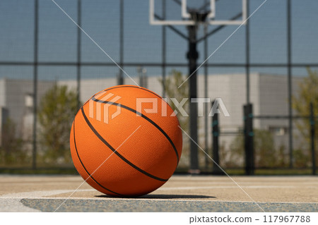Basketball orange ball lies at outdoor public basketball court. Sports gear without people. Template, sport background. Close up. 117967788