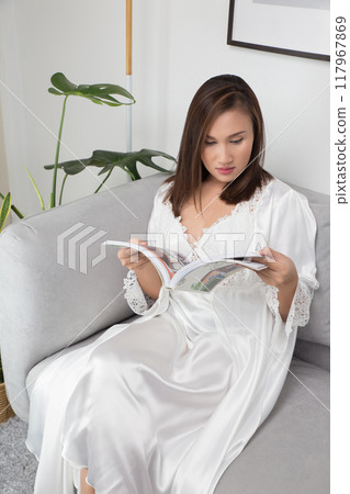A woman in a silk nightgown reads a magazine leisurely. A woman in a silk nightgown reads a magazine leisurely. 117967869
