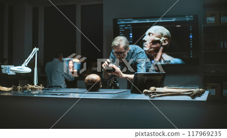 Mature archaeologist photographs fossil skull in archaeological lab with camera 117969235