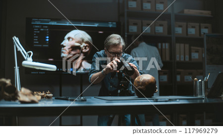 Mature archaeologist takes photo of prehistoric human skull using camera 117969279