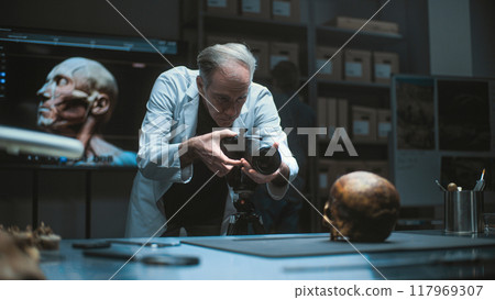 Senior archaeologist takes photo of prehistoric human skull with professional camera 117969307