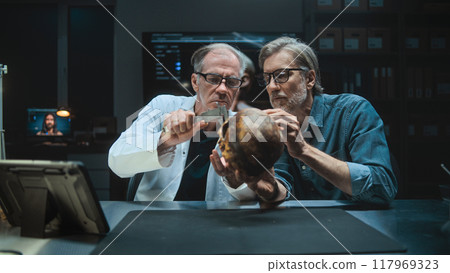 Two archaeologists talk and study skull of ancient extinct human, use tablet computer Two archaeologists talk and study skull of ancient extinct human, use tablet computer 117969323