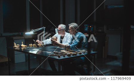 Two archaeologists take measurements of ancient human skull, use tablet computer 117969409