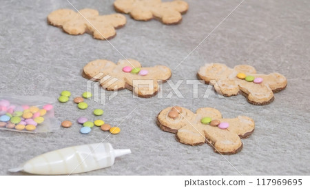 woman's hands decorating a gingerbread man-shaped Christmas cake with white icing and colored caramels, close-up woman's hands decorating a gingerbread man-shaped Christmas cake with white icing and colored caramels, close-up 117969695